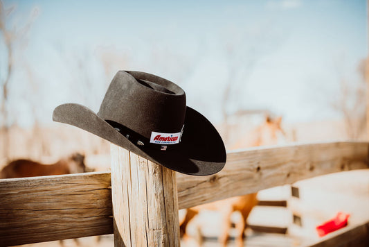 An American Brand black hat sits atop a wooden fence post on a ranch, showcasing Western Wear.